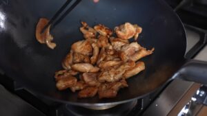 Sliced Chicken Being Stir-Fried in A Black Wok on A Stovetop