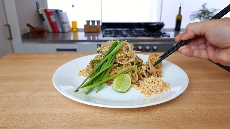 A Plate of Homemade Chicken Pad Thai with Lime, Bean Sprouts, Green Onions, and Crushed Peanuts, with Chopsticks Ready to Serve