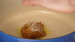 A spoonful of curry paste is sizzling in a pot with coconut milk, starting the base for the Khao Soi broth