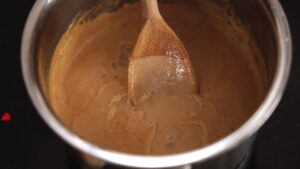 Satay sauce being stirred with a wooden spoon in a saucepan