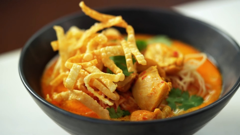 A bowl of Khao Soi featuring tender chicken, crispy fried noodles, and fresh cilantro in a rich, creamy curry broth